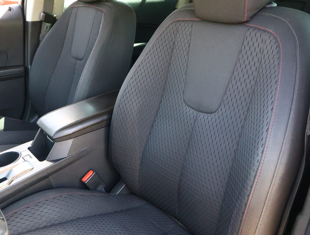 Front car seats with black perforated fabric and red contrast stitching, center console between them with cup holders visible.