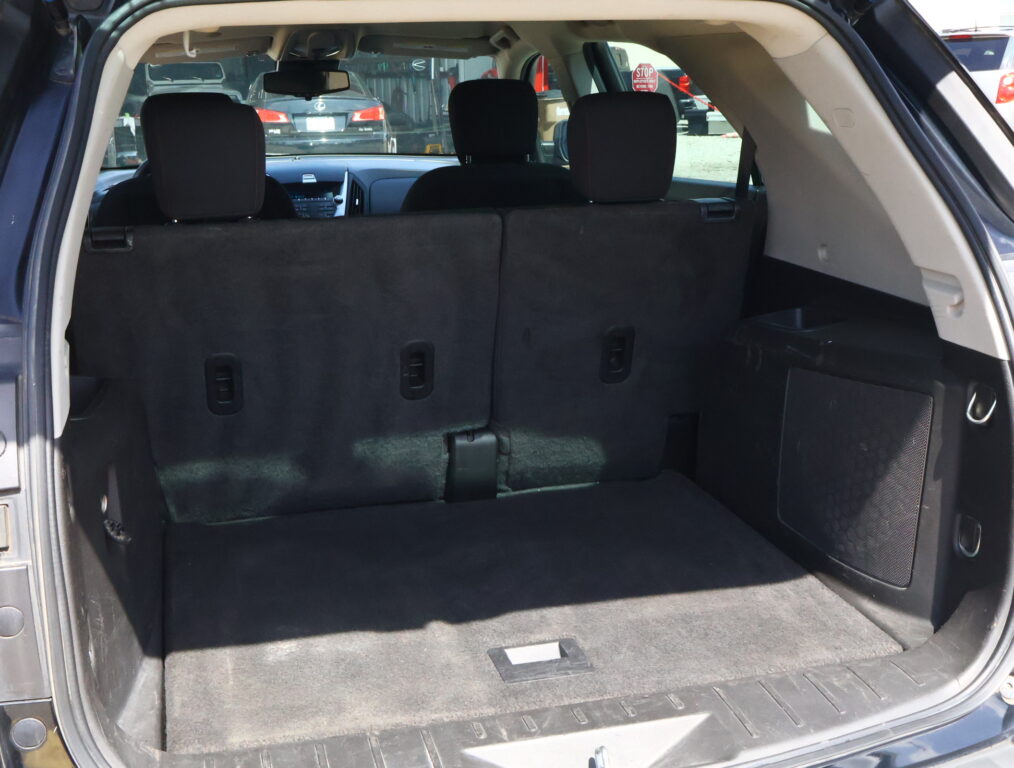SUV cargo area with rear hatch open and third-row seats upright, dark interior and carpeting