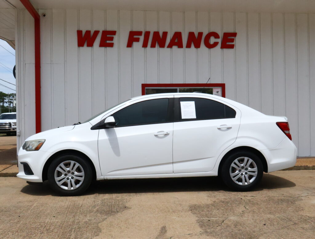 White sedan parked in front of a light-gray wall with large red WE FINANCE letters behind it