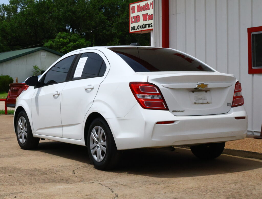 White Chevrolet sedan parked in a lot beside a white building with red trim; papers visible on the rear-side window