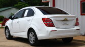 White Chevrolet sedan parked in a lot beside a white building with red trim; papers visible on the rear-side window