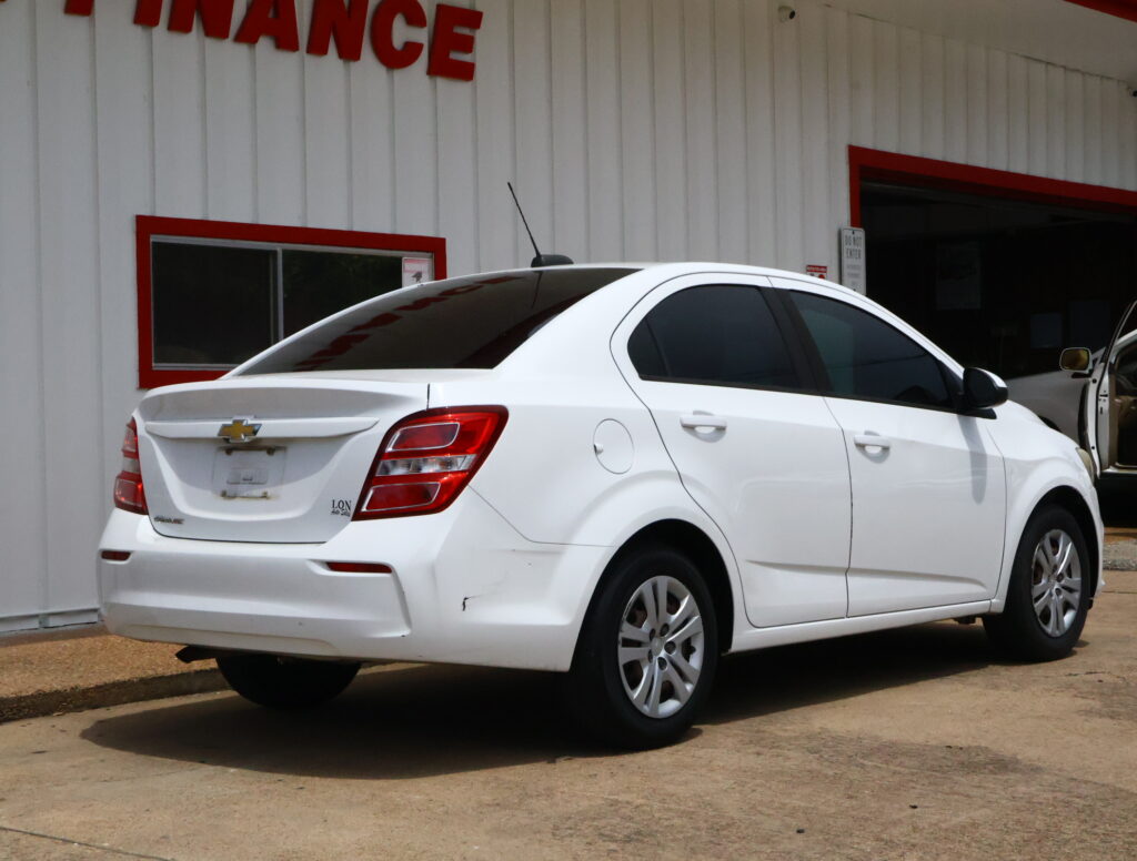 White Chevrolet sedan parked in front of a pale building with red window frames and trims.