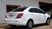 White Chevrolet sedan parked in front of a pale building with red window frames and trims.