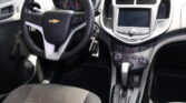Interior of a Chevrolet car: steering wheel with Chevy emblem, instrument cluster, and center infotainment screen above climate controls.