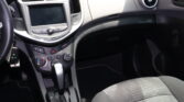 Interior of a car cabin showing the center touchscreen, climate controls, and gear shifter beside a round passenger-side air vent, with part of the dashboard visible.