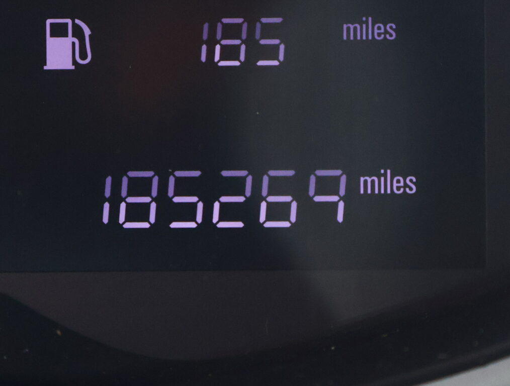 Close-up of a car dashboard: a purple fuel-pump icon on the left and a purple digital readout showing miles, likely an odometer/trip display.