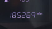 Close-up of a car dashboard: a purple fuel-pump icon on the left and a purple digital readout showing miles, likely an odometer/trip display.