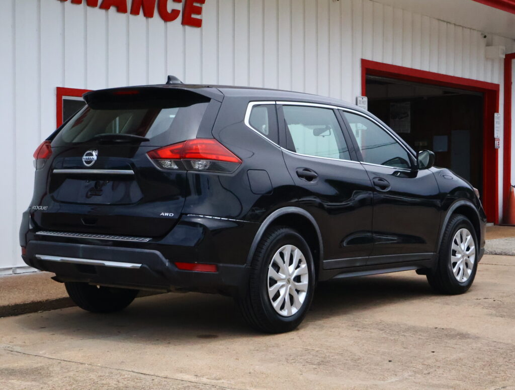 Rear three-quarter view of a black Nissan Rogue SUV parked in front of a white building with red trim doors and accents.