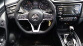 Interior view of a car cockpit showing a Nissan steering wheel, instrument cluster, and central touchscreen with climate and audio controls.