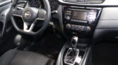 Interior of a Nissan car: steering wheel left, dashboard gauges, and center console with display screen visible.