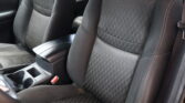 Front interior of a car showing two black fabric seats with stitched patterns, center console, and visible red seat belt buckle between them.