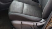 Front passenger seat in a car, dark gray fabric with subtle stripes and a red seat belt buckle nearby.