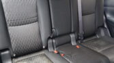 Rear car seat in dark fabric with three seating positions and visible seat belts on a black interior.