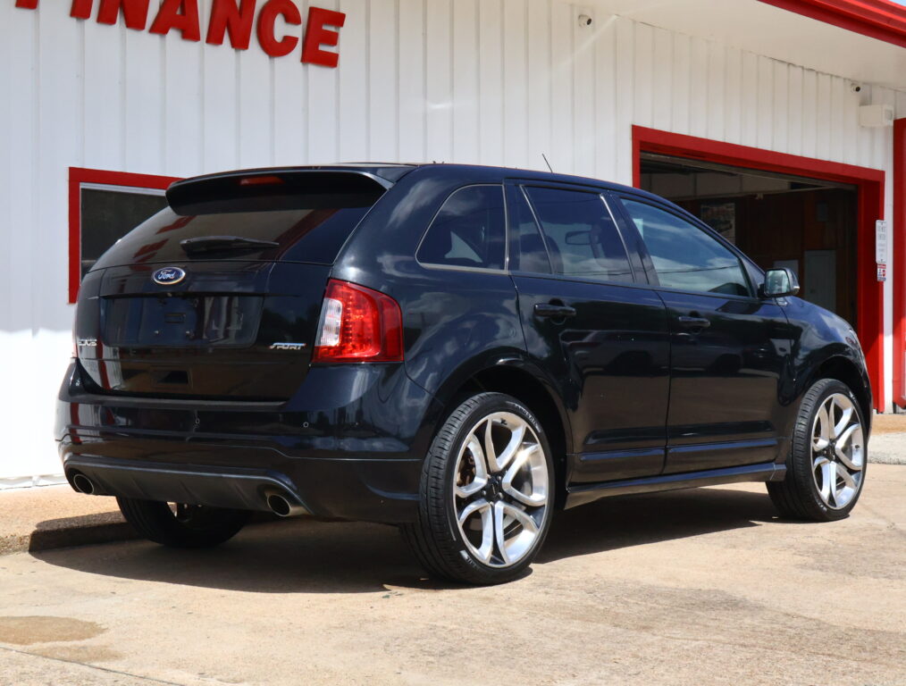 Black Ford Edge SUV parked in front of a white building with red trim and an open service bay door behind it.