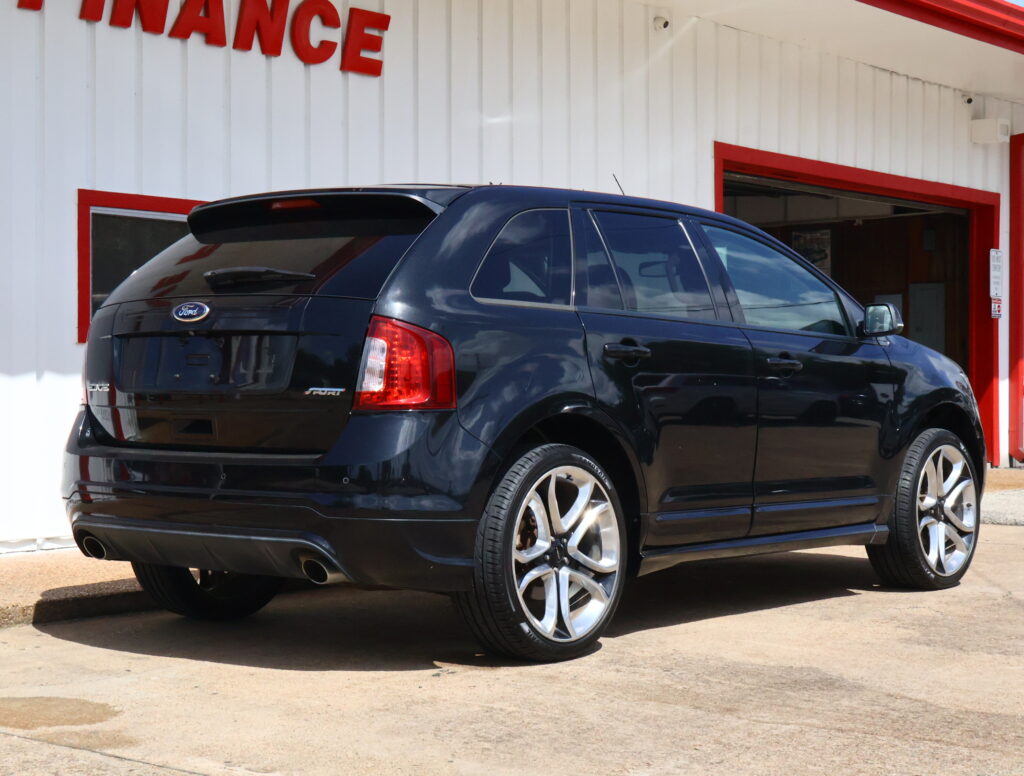 Black Ford Edge SUV parked in front of a white building with red trim and an open service bay door behind it.