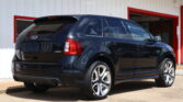 Black Ford Edge SUV parked in front of a white building with red trim and an open service bay door behind it.