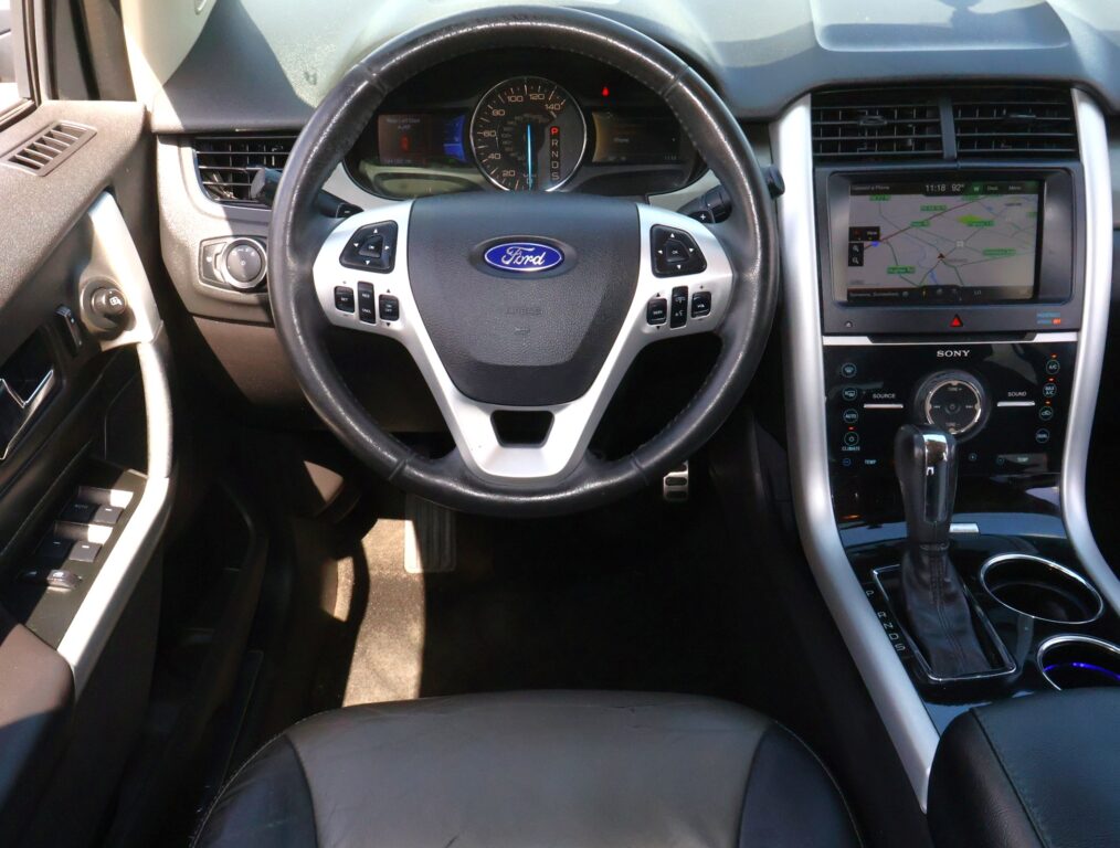 Interior view of a Ford car cabin focusing on the steering wheel with Ford emblem, center console, and a navigation screen to the right.