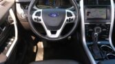 Interior view of a Ford car cabin focusing on the steering wheel with Ford emblem, center console, and a navigation screen to the right.
