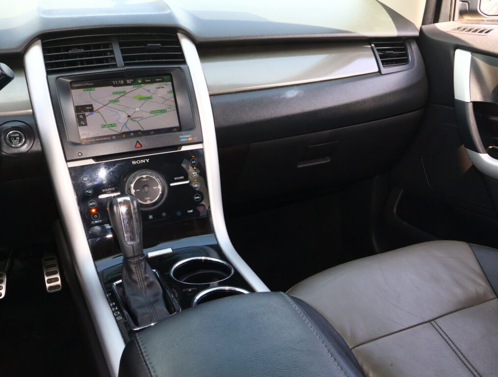 Center console of a car with a touchscreen navigation showing a map, gear shifter in front, and cup holders nearby