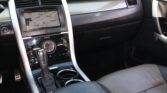 Center console of a car with a touchscreen navigation showing a map, gear shifter in front, and cup holders nearby