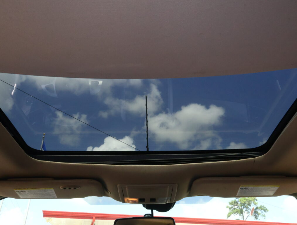 View through an open sunroof: blue sky with white clouds seen from inside a car.
