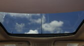 View through an open sunroof: blue sky with white clouds seen from inside a car.