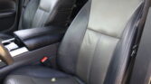 Front seats of a car with black leather upholstery and white stitching, center console visible around them.