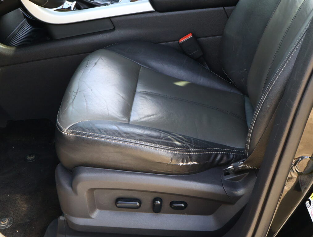 Black leather car seat with visible wear and scratches, side adjustment controls in foreground.