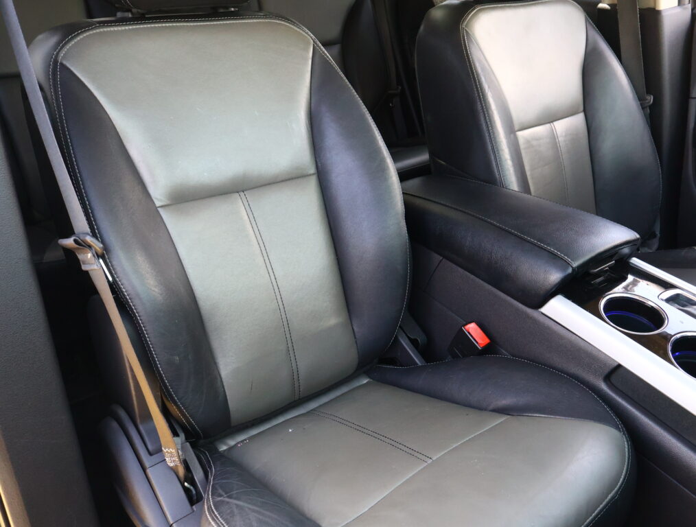 Front car seats in black leather with light stitching and a center console with cupholders visible between them, inside a vehicle interior.