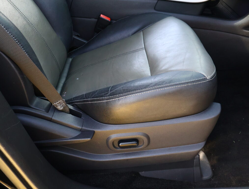 Close-up of a black leather car seat with white stitching and a visible seat belt at the left side.
