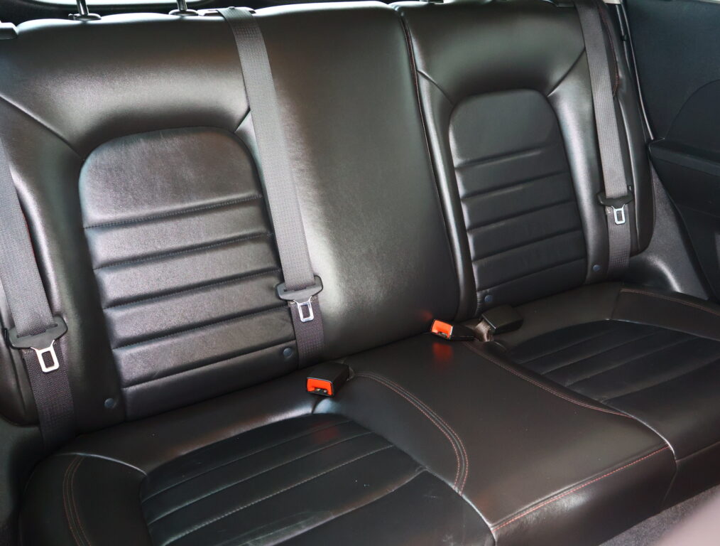 Black leather rear car seat with three seating positions and visible three-point seat belts.