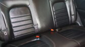 Black leather rear car seat with three seating positions and visible three-point seat belts.