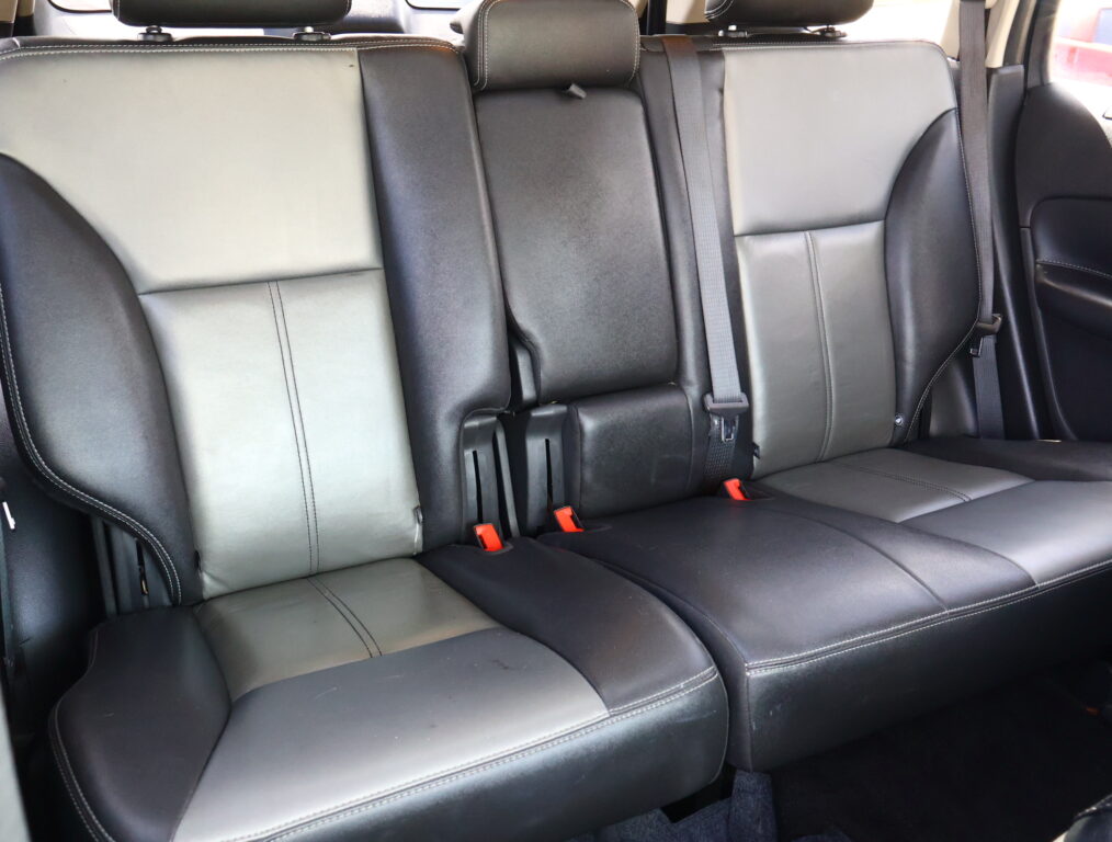 Rear car seats in black leather with light stitching and three seat positions, visible seat belts and headrests.