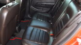 Rear passenger seat area of a black leather car interior with red stitching, showing the seatbelt and door panel.