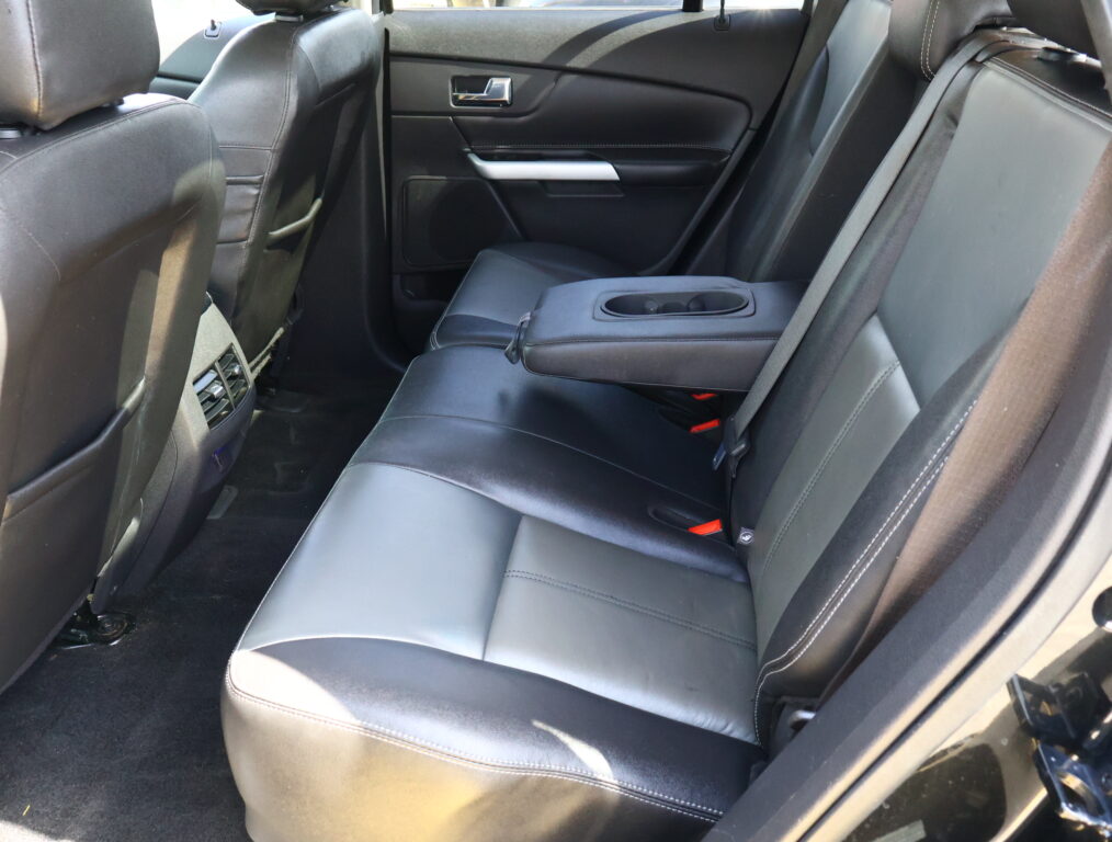 Rear car seat interior in black leather with a folded center armrest and cup holders, door panel, and rear vents from the passenger side view