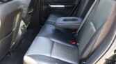 Rear car seat interior in black leather with a folded center armrest and cup holders, door panel, and rear vents from the passenger side view