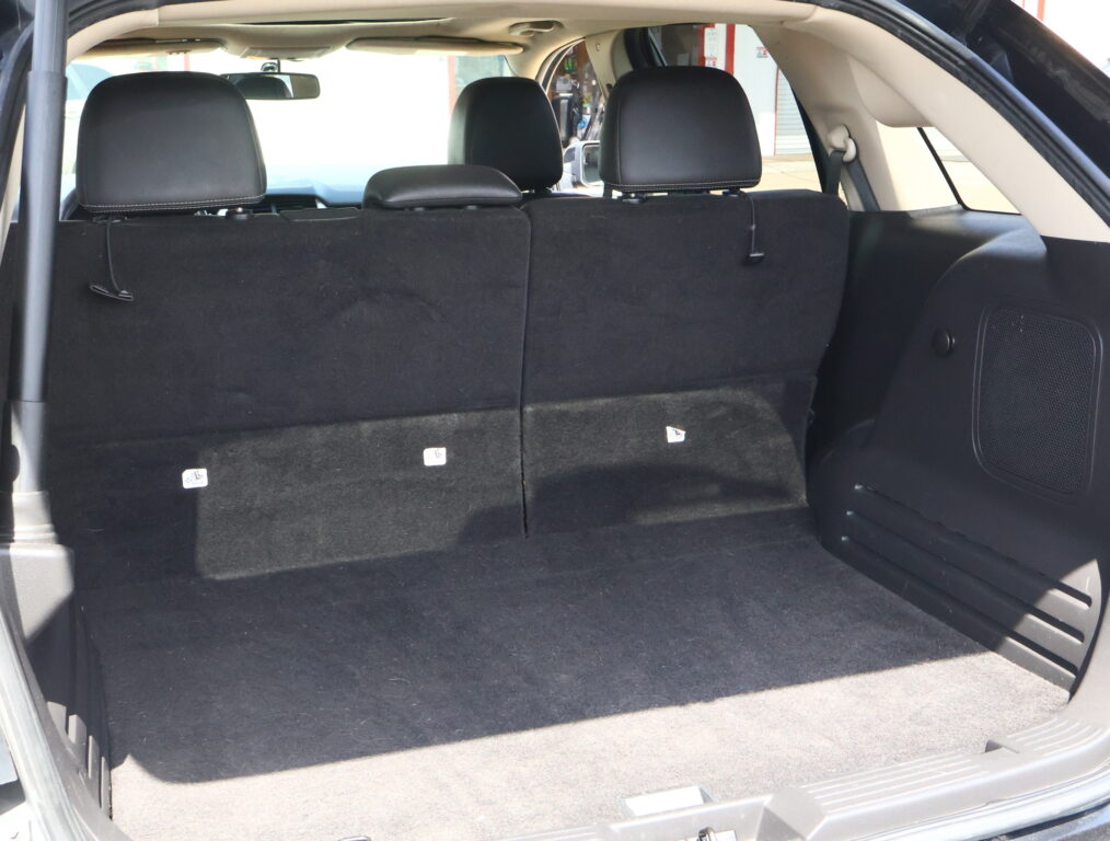 Open SUV trunk showing black fabric cargo area with upright rear seats and headrests; small label icons on seatbacks visible.