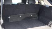 Open SUV trunk showing black fabric cargo area with upright rear seats and headrests; small label icons on seatbacks visible.