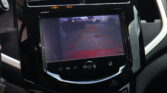 In-car infotainment screen showing a rearview camera feed with orange parking guide lines and the message 'Check Surroundings For Safety'.
