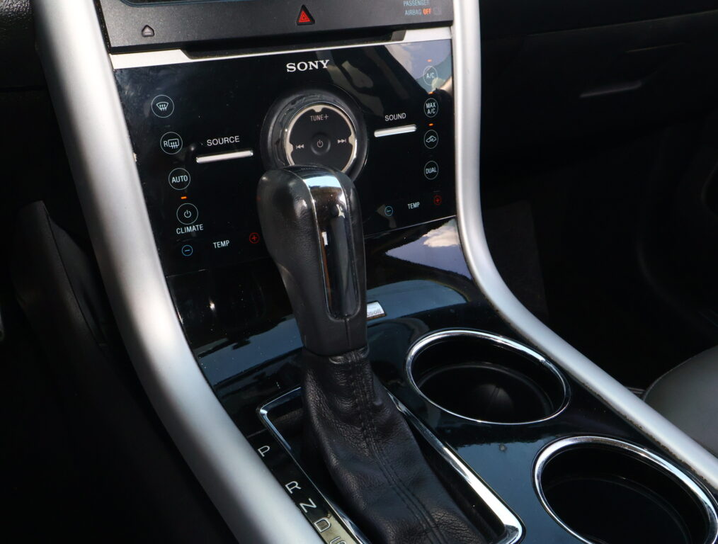 Close-up of a car center console with a leather gear shifter and glossy black control panel labeled SONY and visible drive modes (P R N D).
