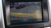 Rearview camera display showing parking guidelines with green, yellow, and red lines and a safety reminder text, 'Please check surroundings for safety.'