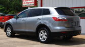 Silver SUV parked in front of a white and red car dealership building with a bold 'WE FINANCE' sign and a large roadside sign advertising 12-month/12k mile LTD warranty next to green trees.