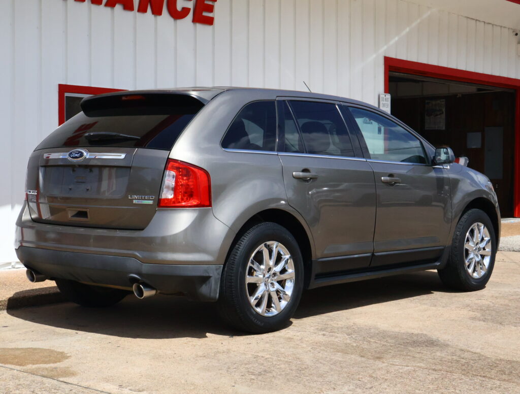 Rear three-quarter view of a silver Ford SUV (Limited) with chrome wheels, parked in front of a white building with red trim and a finance sign partially visible above.