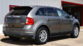 Rear three-quarter view of a silver Ford SUV (Limited) with chrome wheels, parked in front of a white building with red trim and a finance sign partially visible above.