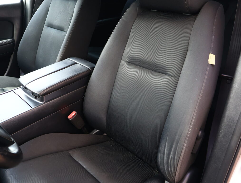 Front car seats in a dark fabric interior, with a center armrest between them and a visible seatbelt buckle.