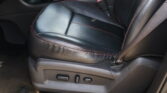 Black leather car seat with red contrast stitching and side-adjustment controls visible on the lower seat side panel, plus a red seat belt buckle nearby.