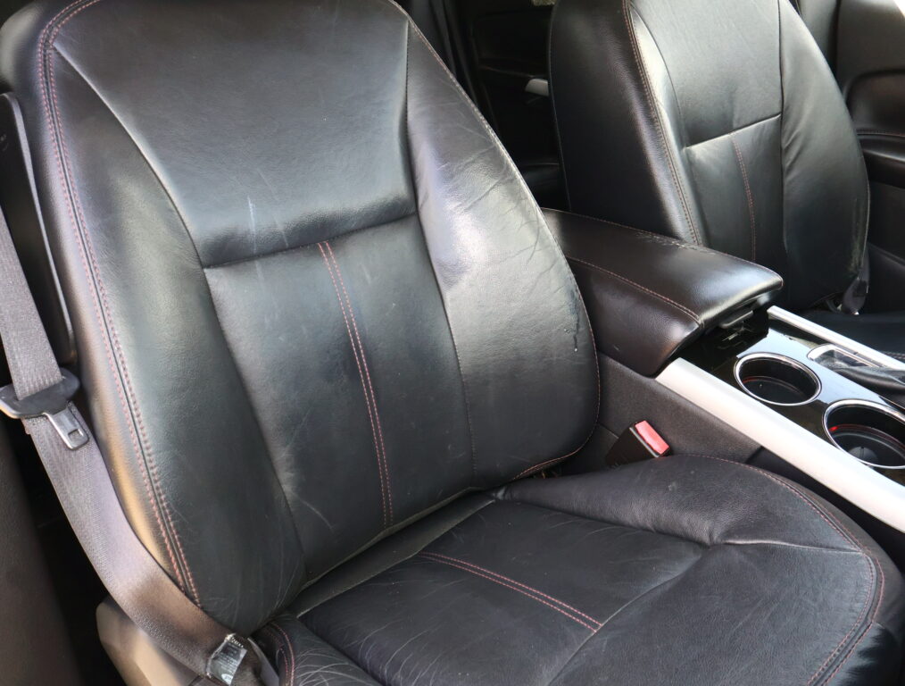 Black leather car seats with red contrast stitching and a center console with cup holders visible between the seats, front interior.