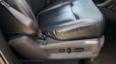 Black leather car seat with red contrast stitches and a seatbelt draped across the seating area; interior controls and center console visible nearby.