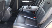 Rear car seating area with black leather seats and red contrast stitching; center armrest is down, revealing built-in cup holders.