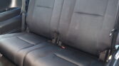 Backseat of a car with black fabric upholstery, showing seat cushions and a hanging seatbelt.